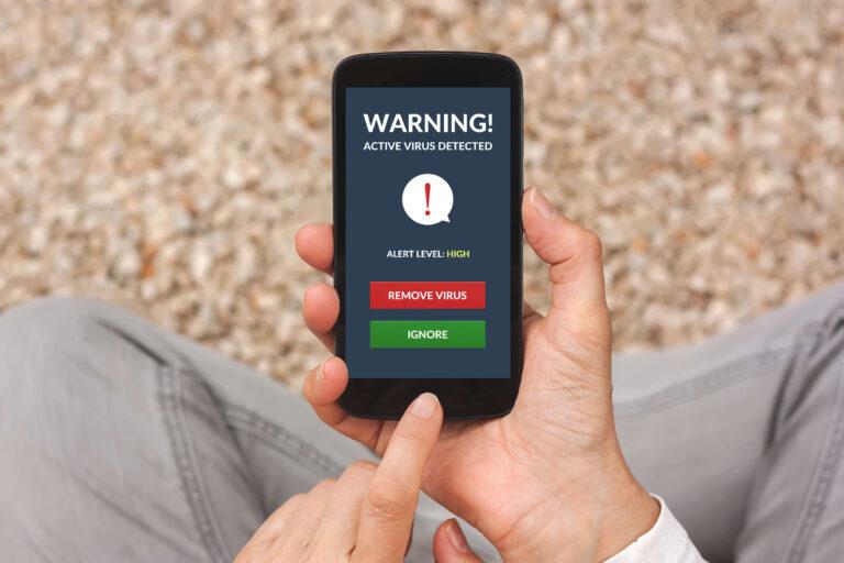 Hands holding smartphone with virus alert on screen.