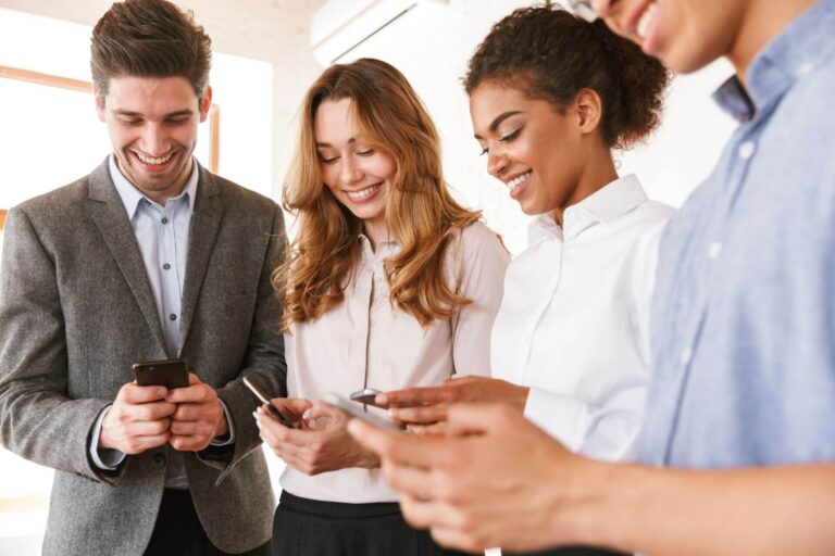 Group of happy young multiethnic businesspeople standing in an office and using mobile phones